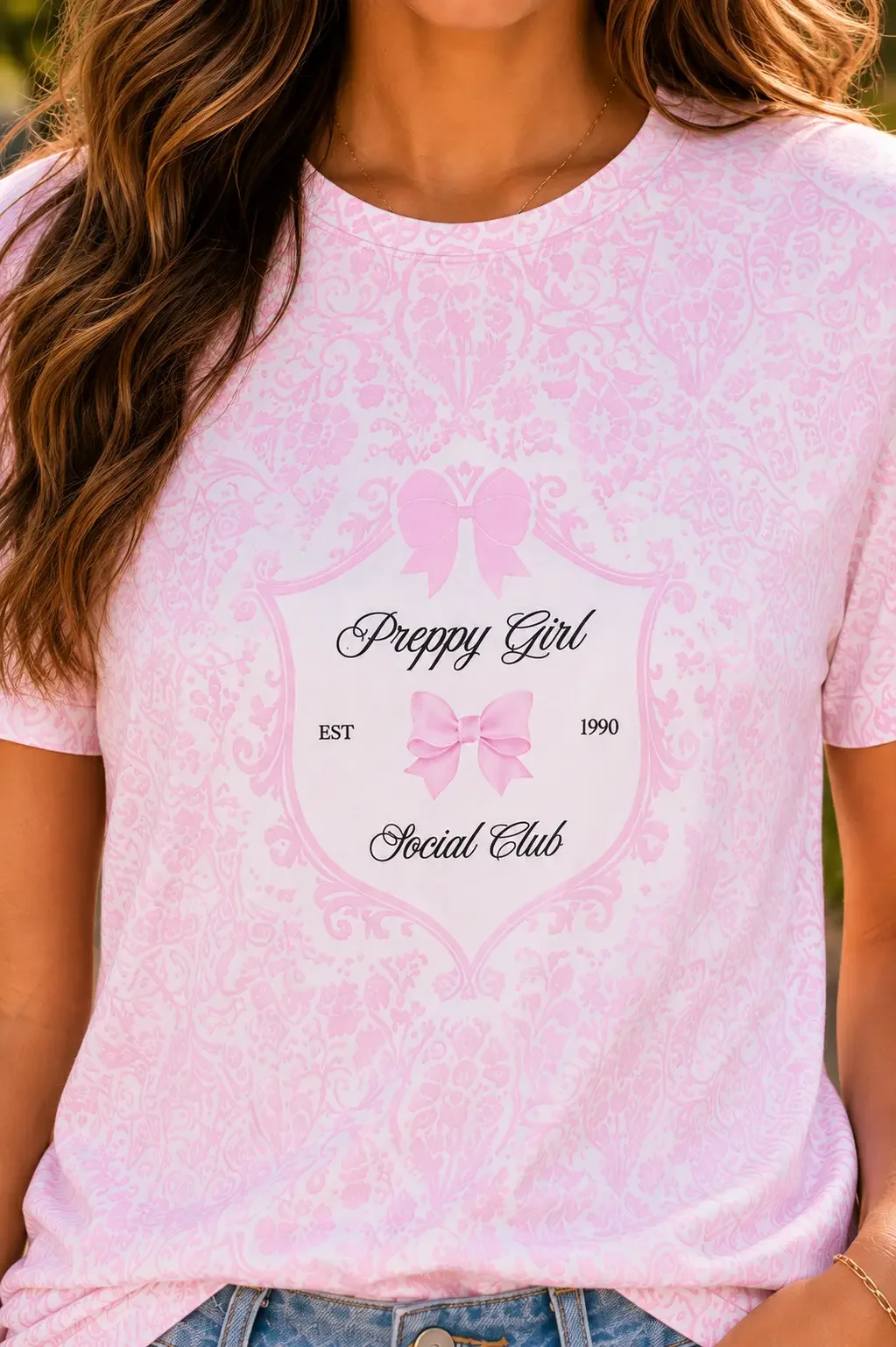Close-up of a pink damask patterned shirt with a crest reading Preppy Girl Social Club and pink bow graphics.
