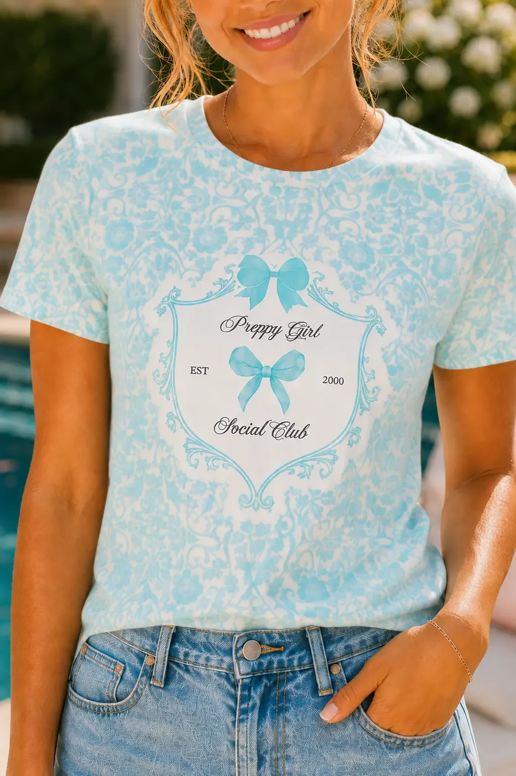 Close-up of a blue damask patterned shirt with a crest reading Preppy Girl Social Club and blue bow graphics.