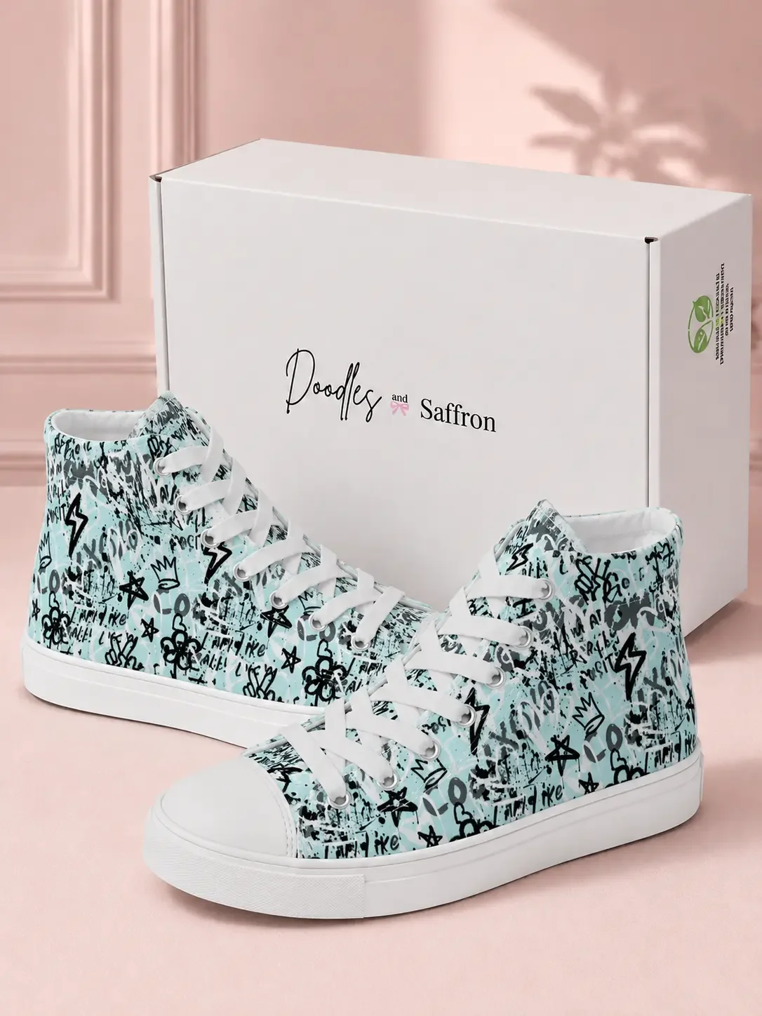A pair of mint green graffiti print high-top sneakers displayed in front of a white Doodles and Saffron shoebox.