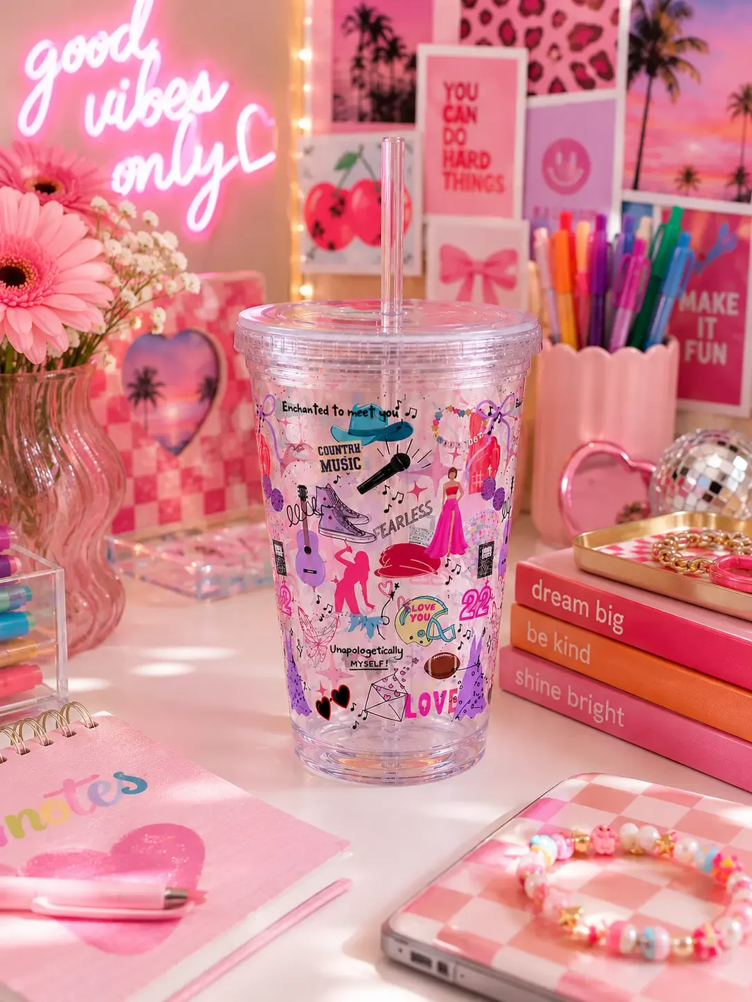 A preppy country pop star tumbler cup in front of a pink gift bag, motivational card, and cosmetic accessories.
