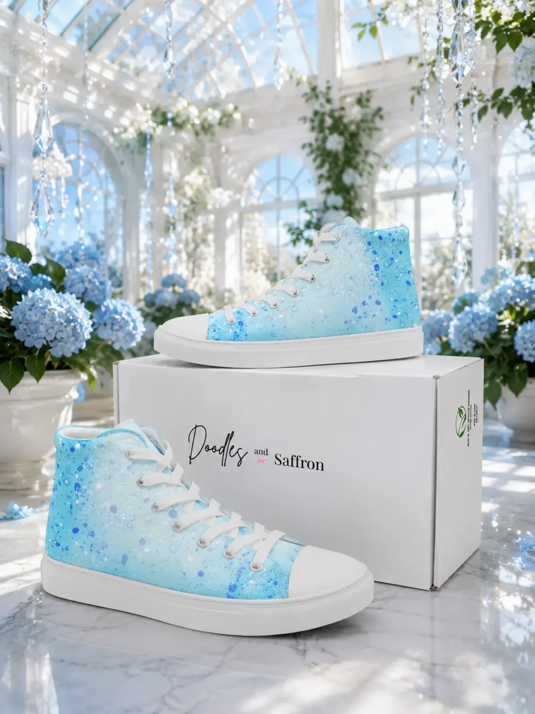 A pair of light blue paint splatter print high-top sneakers displayed with a Doodles and Saffron shoebox inside a greenhouse.