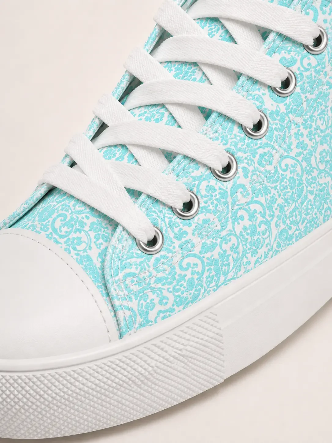 Close-up of a white canvas high-top sneaker featuring an intricate mint green lace pattern and white laces.