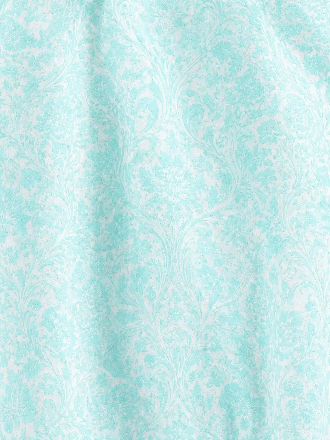 Zoomed-in macro shot of a soft mint green floral damask brocade pattern printed on textured white apparel fabric.