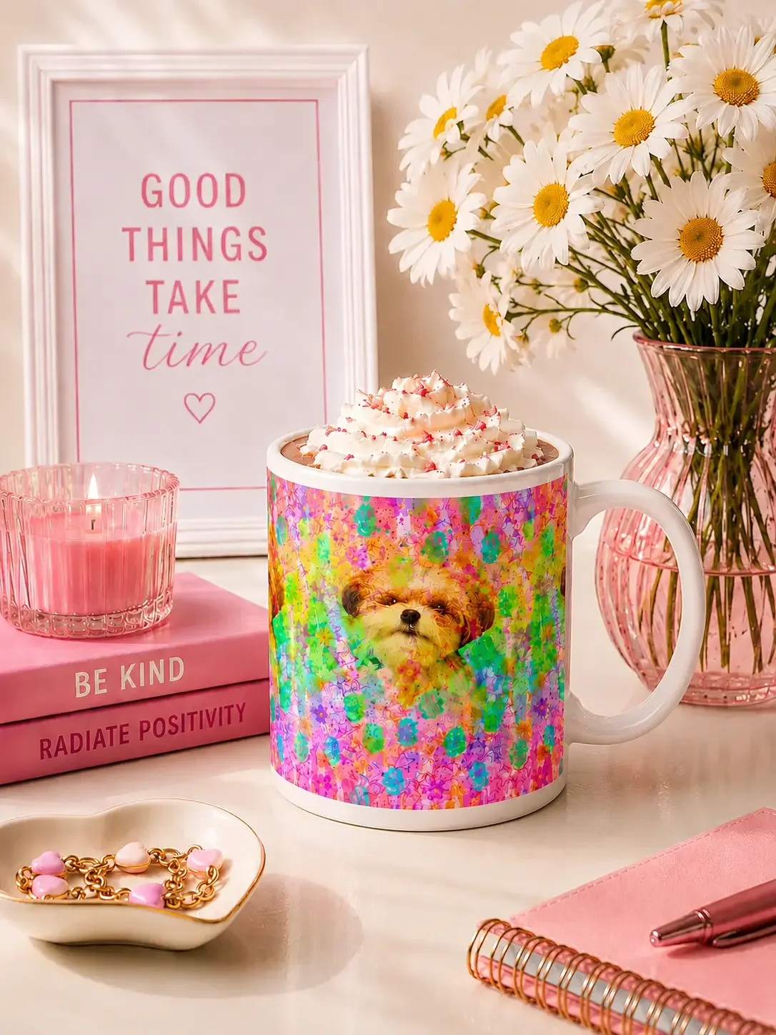 Watercolor dog mug filled with whipped cream on a desk with pink books, a lit candle, and white daisies.