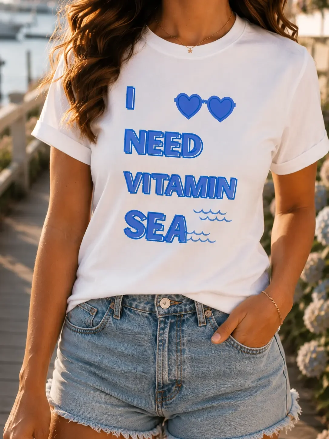 Close-up view of a woman wearing a white crew neck t-shirt with a blue I Need Vitamin Sea graphic and blue denim shorts.