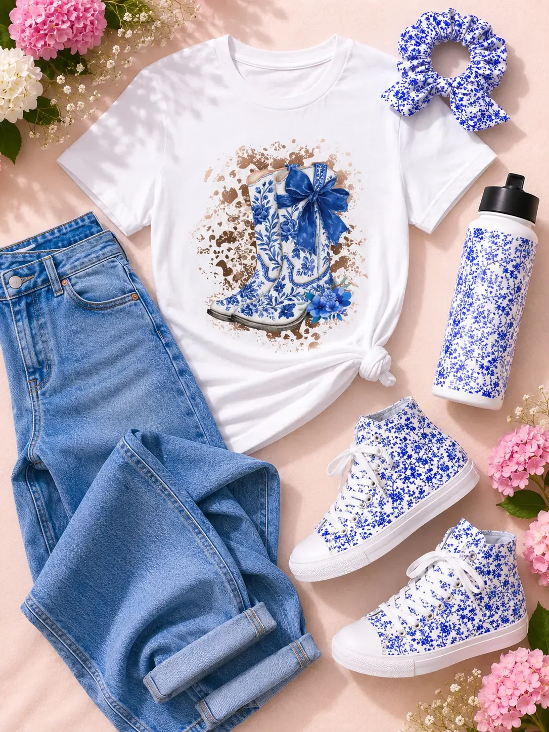 Flat lay arrangement of a white cowboy boots t-shirt, blue jeans, floral sneakers, water bottle, and scrunchie.