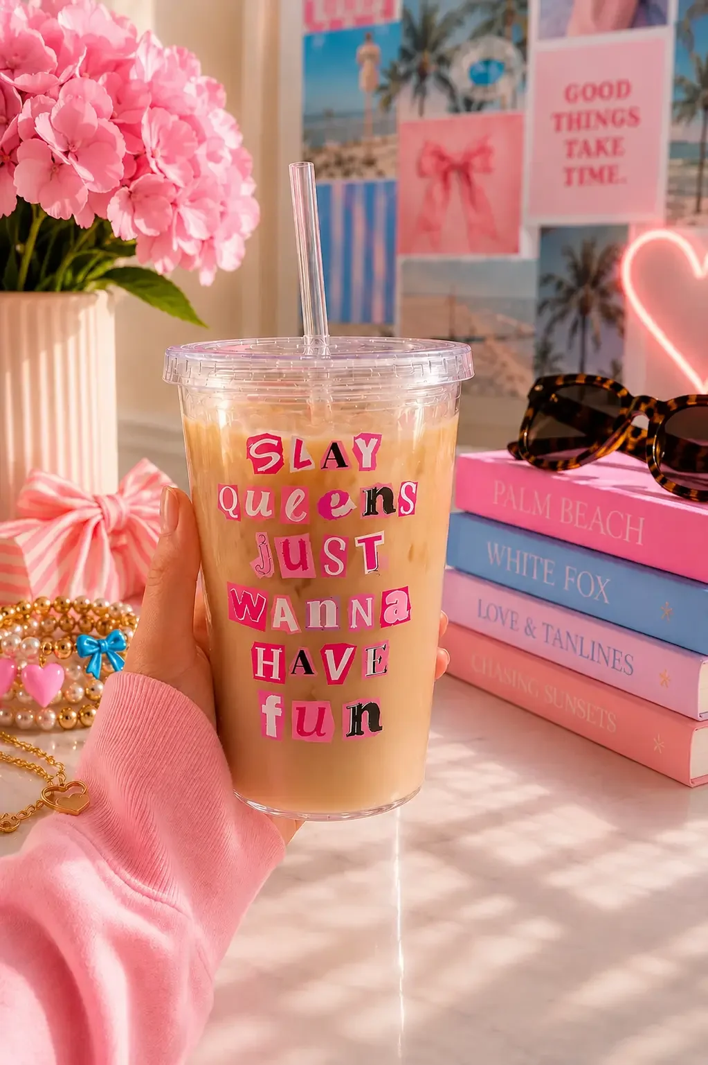 Hand holding a preppy "Slay Queens Just Wanna Have Fun" tumbler cup with iced coffee on an aesthetic pink desk setup.