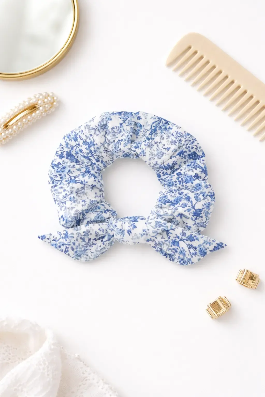 Flat lay display of a white hair scrunchie with a blue floral pattern, styled next to a hair comb, mirror, and clips. (Copy)