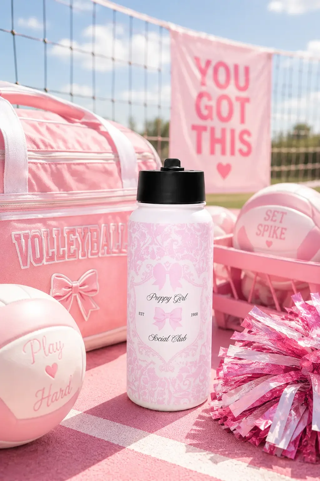 A pink damask Social Club water bottle standing next to a pink volleyball duffel bag, volleyballs, and pink pom-poms.