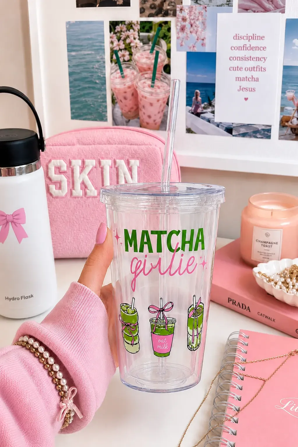Hand holding a clear preppy "Matcha Girlie" tumbler cup on an aesthetic pink desk next to a white Hydro Flask.