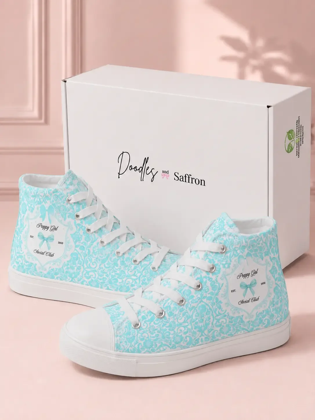 A pair of mint green lace print high-top canvas sneakers displayed in front of a white Doodles and Saffron shoebox.
