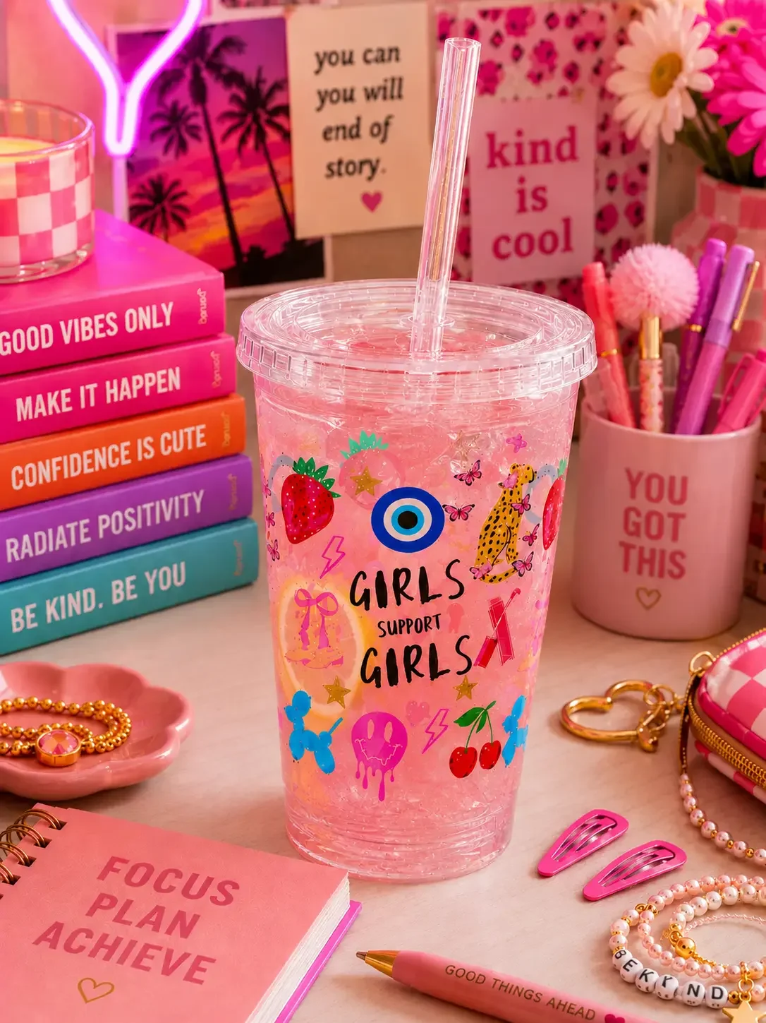 A preppy "Girls Support Girls" doodle tumbler cup filled with a pink iced beverage on an aesthetic pink desk setup.
