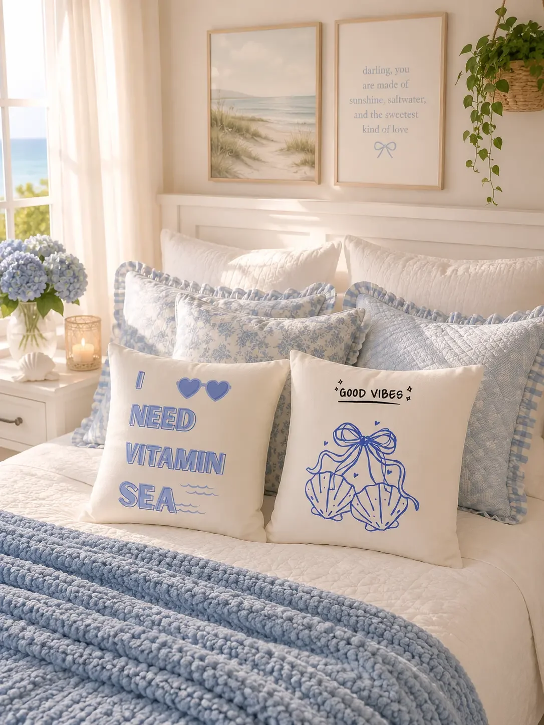 A pair of white square pillows printed with I Need Vitamin Sea text and a blue seashell bow ribbon sketch displayed on a decorated bed.