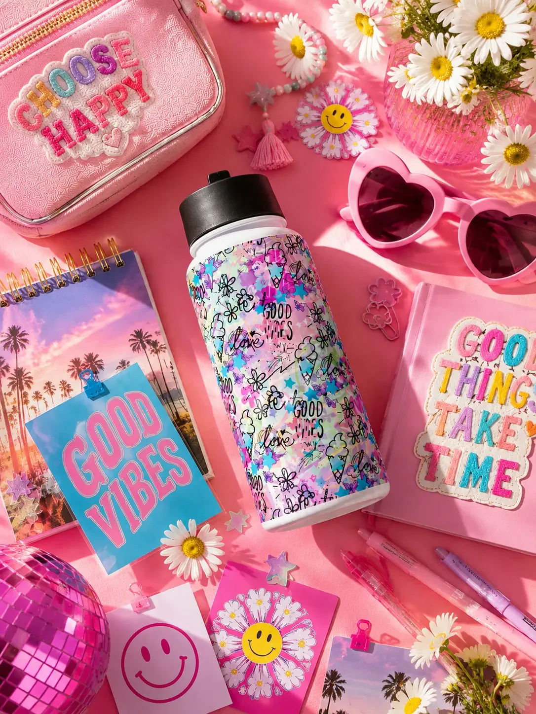 Flat lay of a colorful doodle print water bottle surrounded by pink school supplies and preppy stationery.