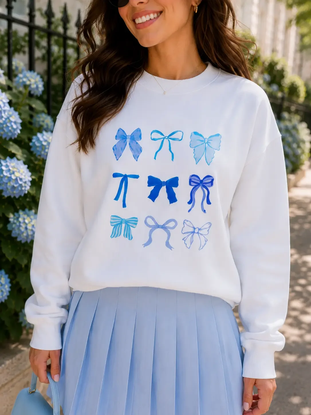 Close-up shot of a white crewneck sweatshirt featuring a graphic grid pattern of nine unique shades and styles of blue ribbon bows.