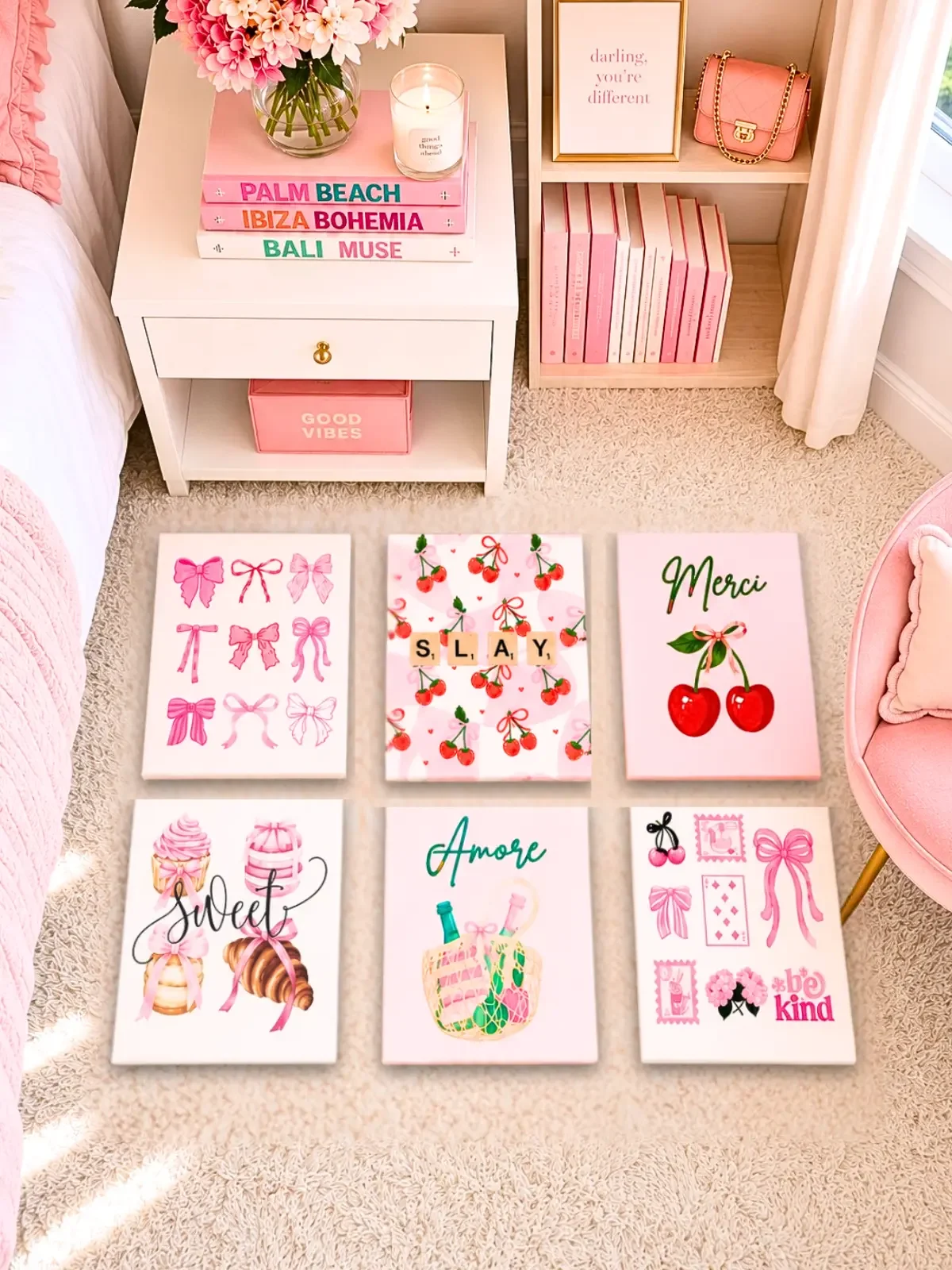Six pink coquette canvas prints featuring bows, cherries, cupcakes, and stamps arranged on a beige bedroom rug.