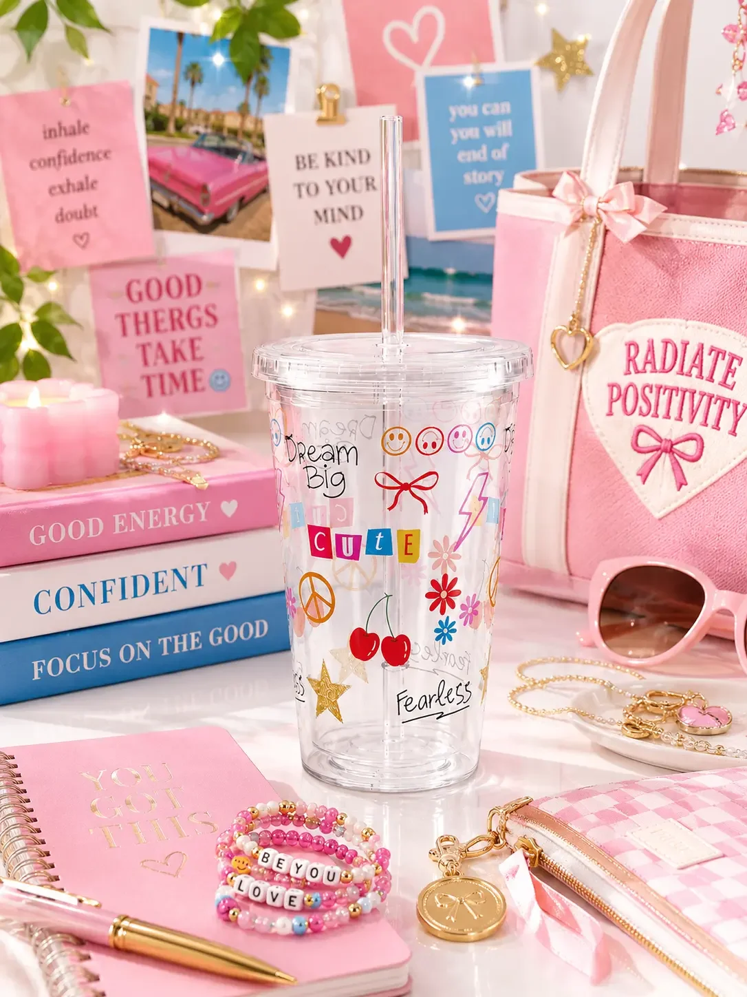 A clear plastic straw tumbler with vibrant preppy Y2K sticker doodles, sitting in a pink desk flat lay setup.