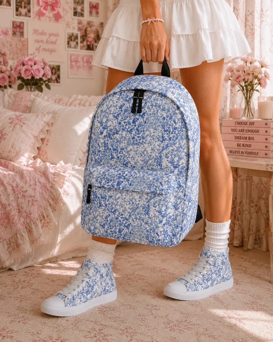Young woman wearing a white skirt and matching blue floral sneakers holds a blue floral print backpack in a bedroom.