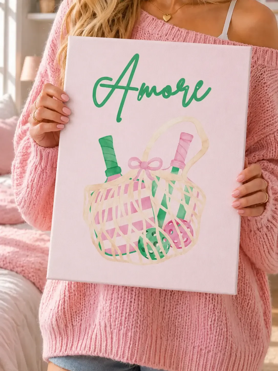 Girl in a pink knit sweater holding an "Amore" canvas art print featuring a watercolor pickleball tote.