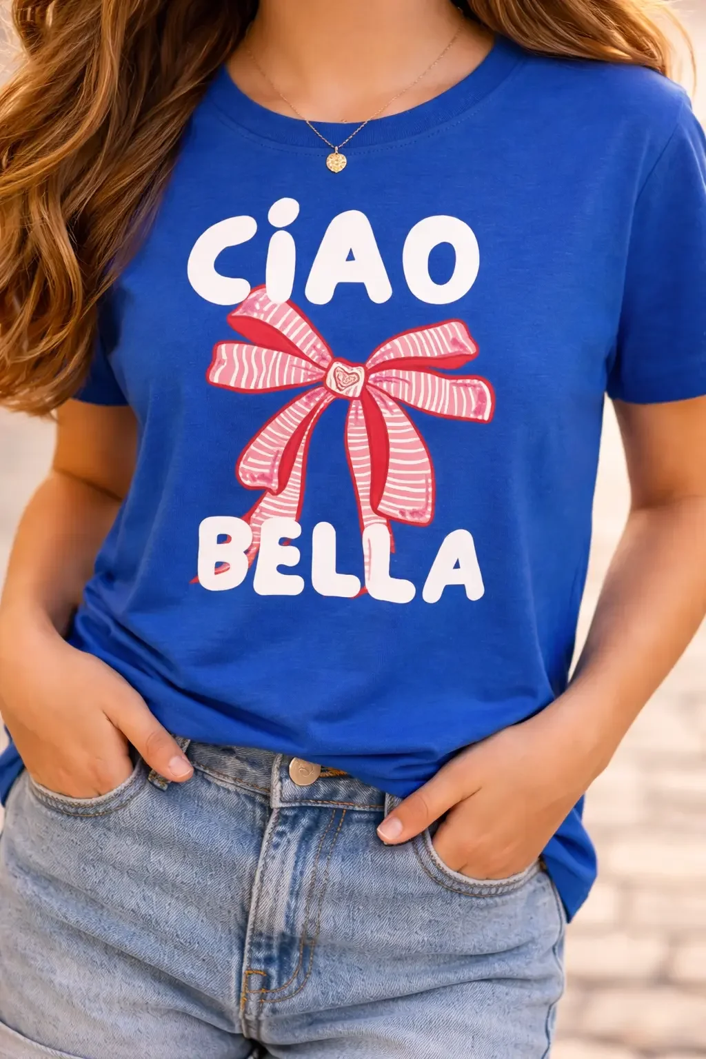 Close-up of a royal blue graphic tee showing the words "Ciao Bella" surrounding a red and pink striped coquette ribbon bow.