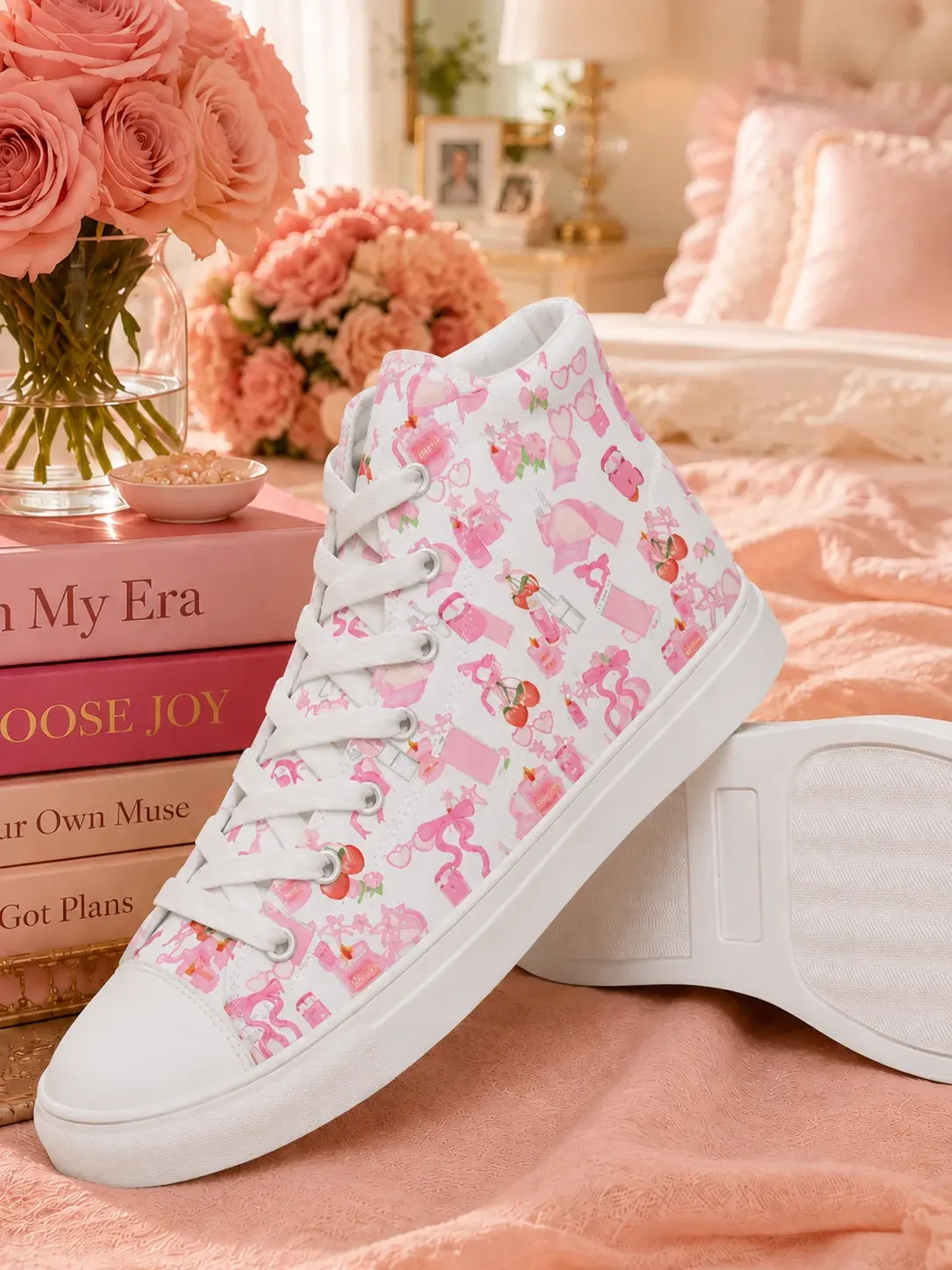 White high-top sneakers with a pink ribbon bow and cherry pattern resting on a bed next to a stack of journals.