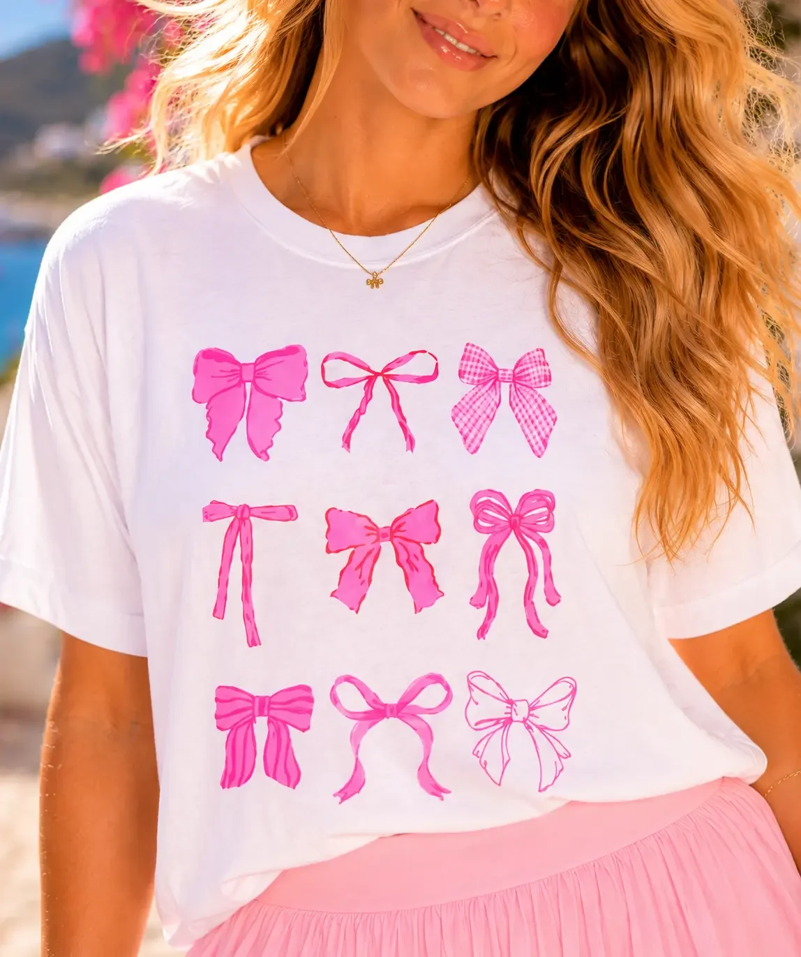 Close-up of a woman wearing a white t-shirt featuring a grid of nine unique pink coquette ribbon bow graphics.
