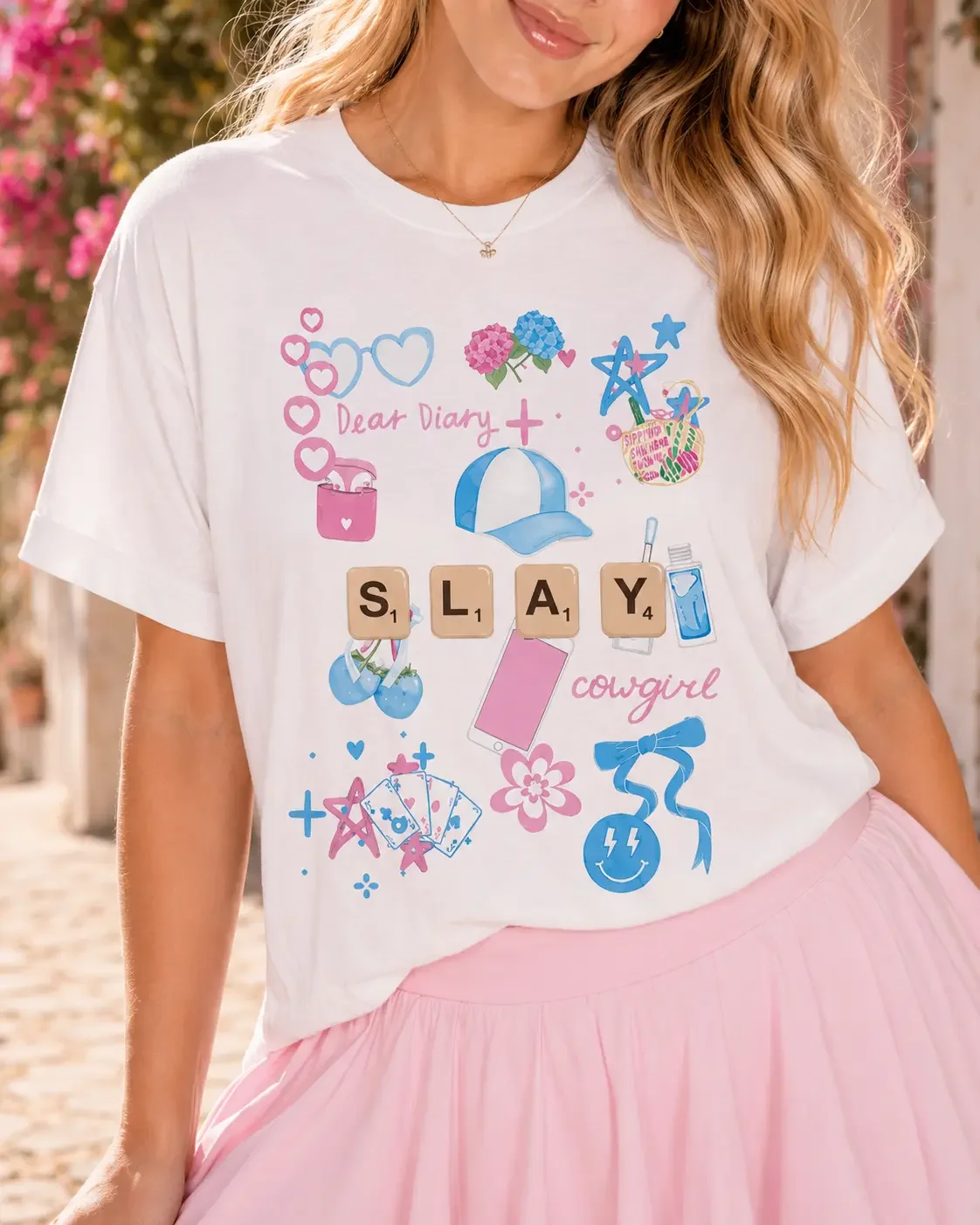 Close-up of a woman wearing a white t-shirt featuring a "Dear Diary Slay Cowgirl" doodle graphic with letter tiles.