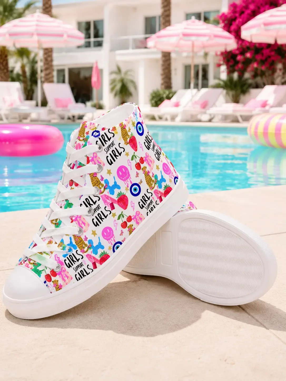 ]White high-top canvas sneakers with a colorful graphic print pattern displayed on the ground next to a resort swimming pool.