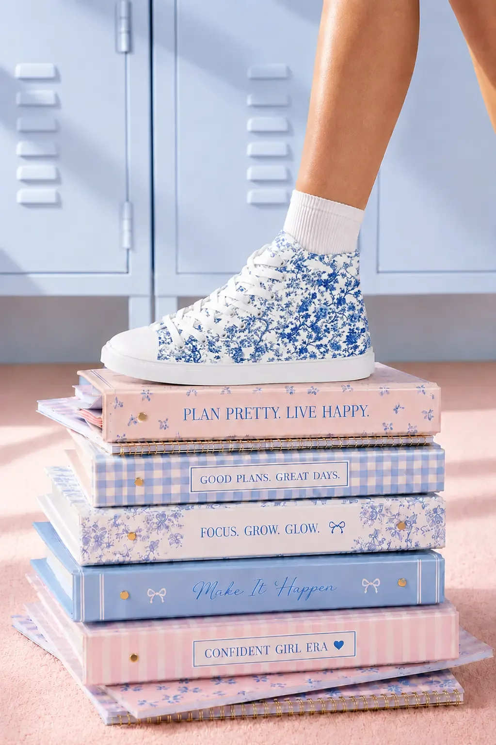 A person wearing a blue floral toile print high-top canvas sneaker stepping on a stack of pastel aesthetic binders.