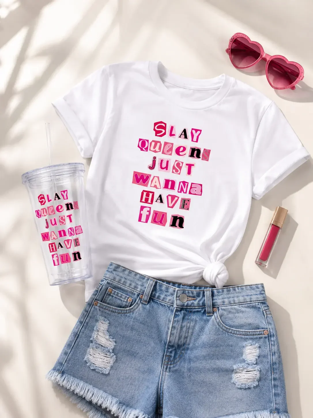 Flat lay outfit display featuring a white Slay Queens graphic tee, distressed denim shorts, a matching tumbler, heart sunglasses, and lip gloss.