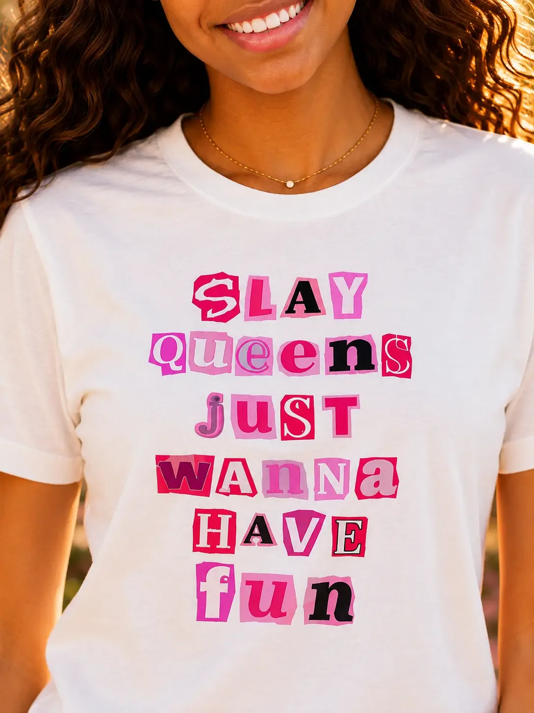 Close-up of a white graphic t-shirt with pink ransom-note style letters reading Slay Queens Just Wanna Have Fun.