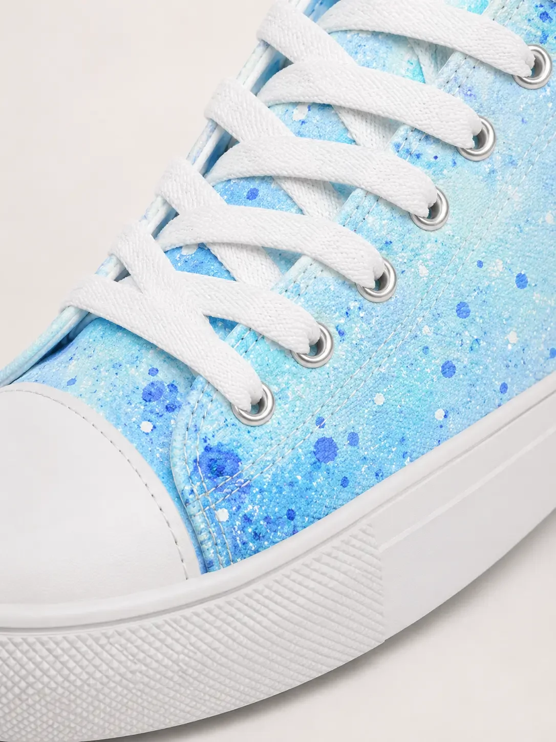 Close-up of a light blue canvas high-top sneaker featuring a vibrant blue paint splatter pattern and white laces.