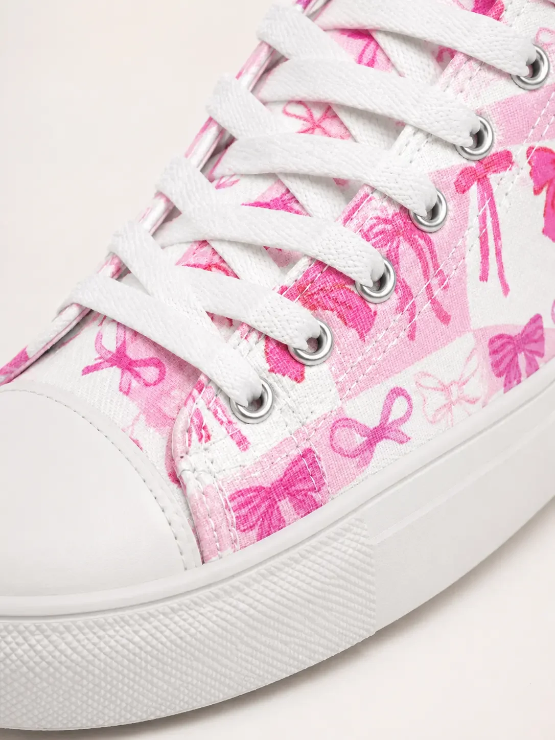 Close-up detail of white canvas laces, rubber sole, and a pink checkered canvas material with a ribbon bow pattern.