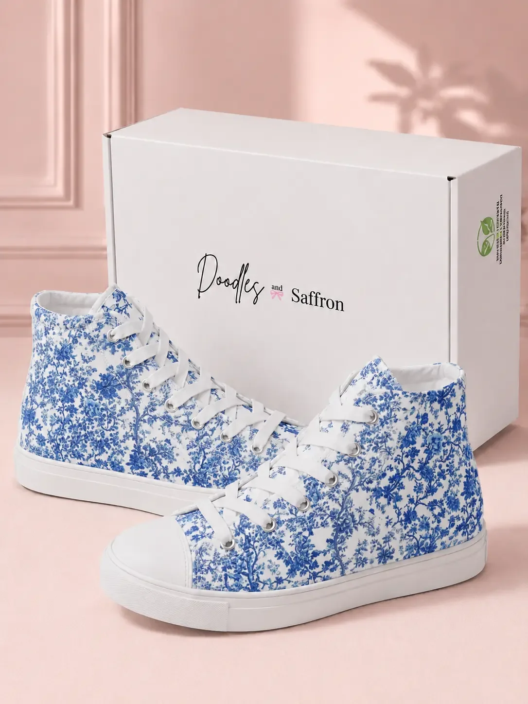A pair of blue floral toile print high-top sneakers displayed in front of a white Doodles and Saffron shoebox.