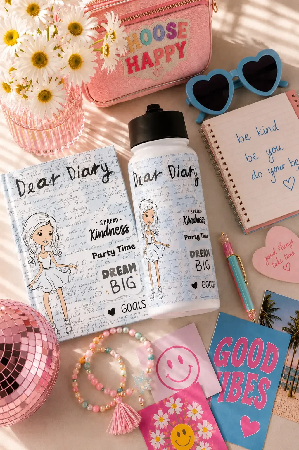 Flat lay of a handwritten Dear Diary water bottle surrounded by pink school supplies and blue heart sunglasses.