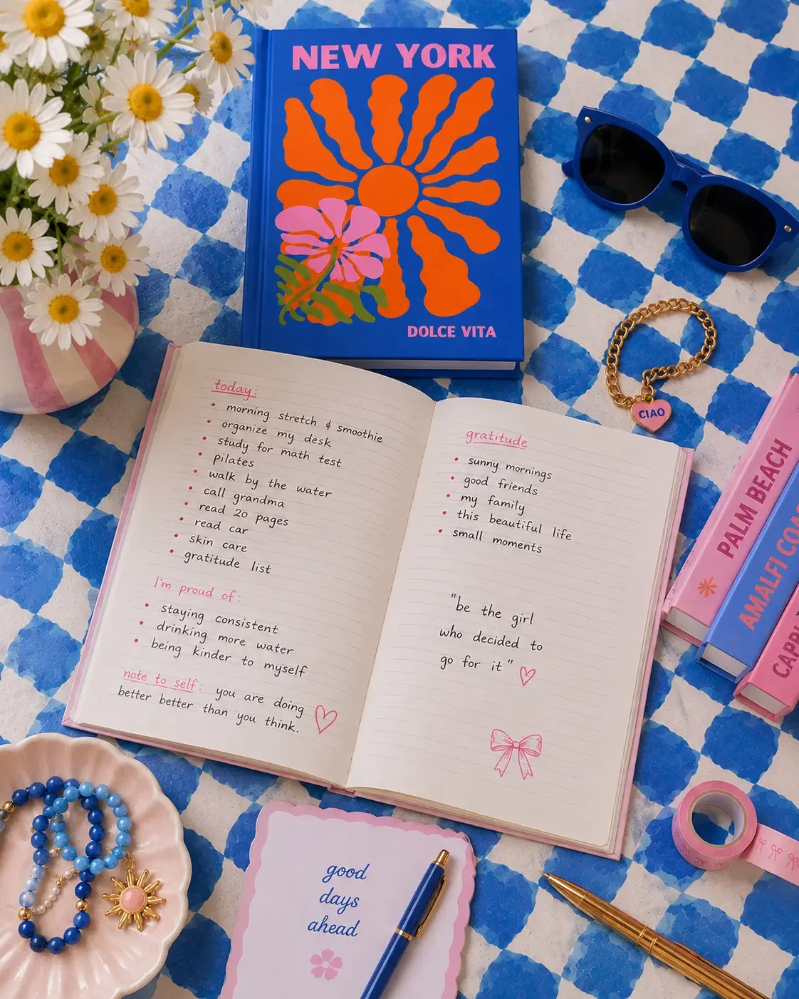 An open journal with a daily self-care checklist and gratitude notes on a blue checkered desk with a New York Dolce Vita notebook.