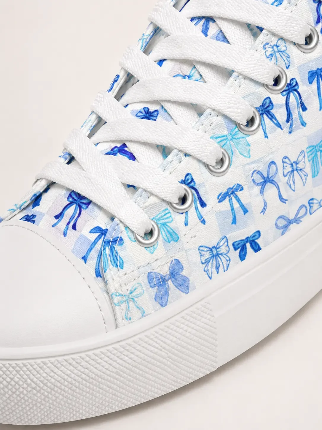 Close-up of a white canvas high-top sneaker featuring a vibrant blue coquette ribbon bow pattern and white laces.