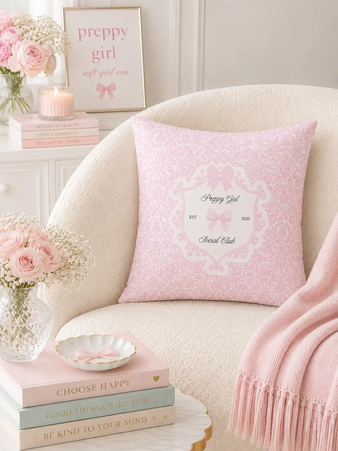 A square pink damask cushion with a white crest and bow details resting on a cream-colored boucle accent chair.
