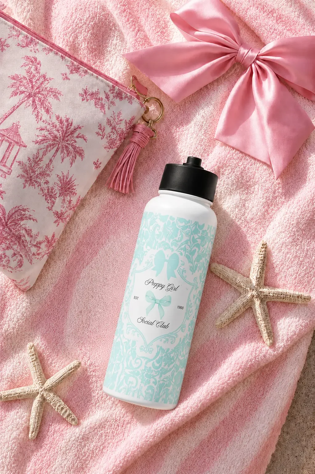 A light blue damask water bottle resting on a pink striped towel next to starfishes, a satin bow, and a toile pouch.