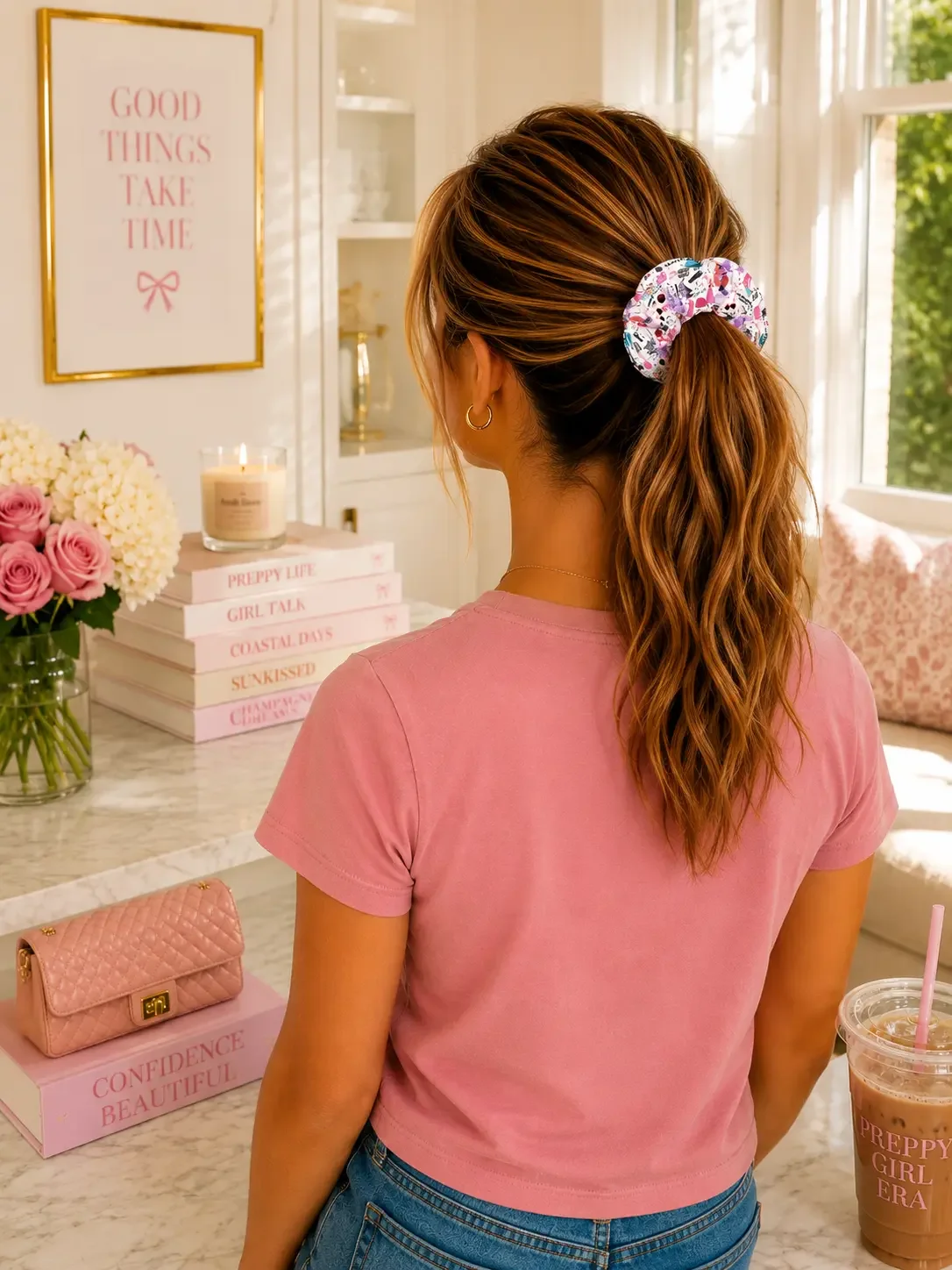Back view of a woman with highlighted brown hair in a high ponytail secured with a Taylor Swift Eras doodle scrunchie.