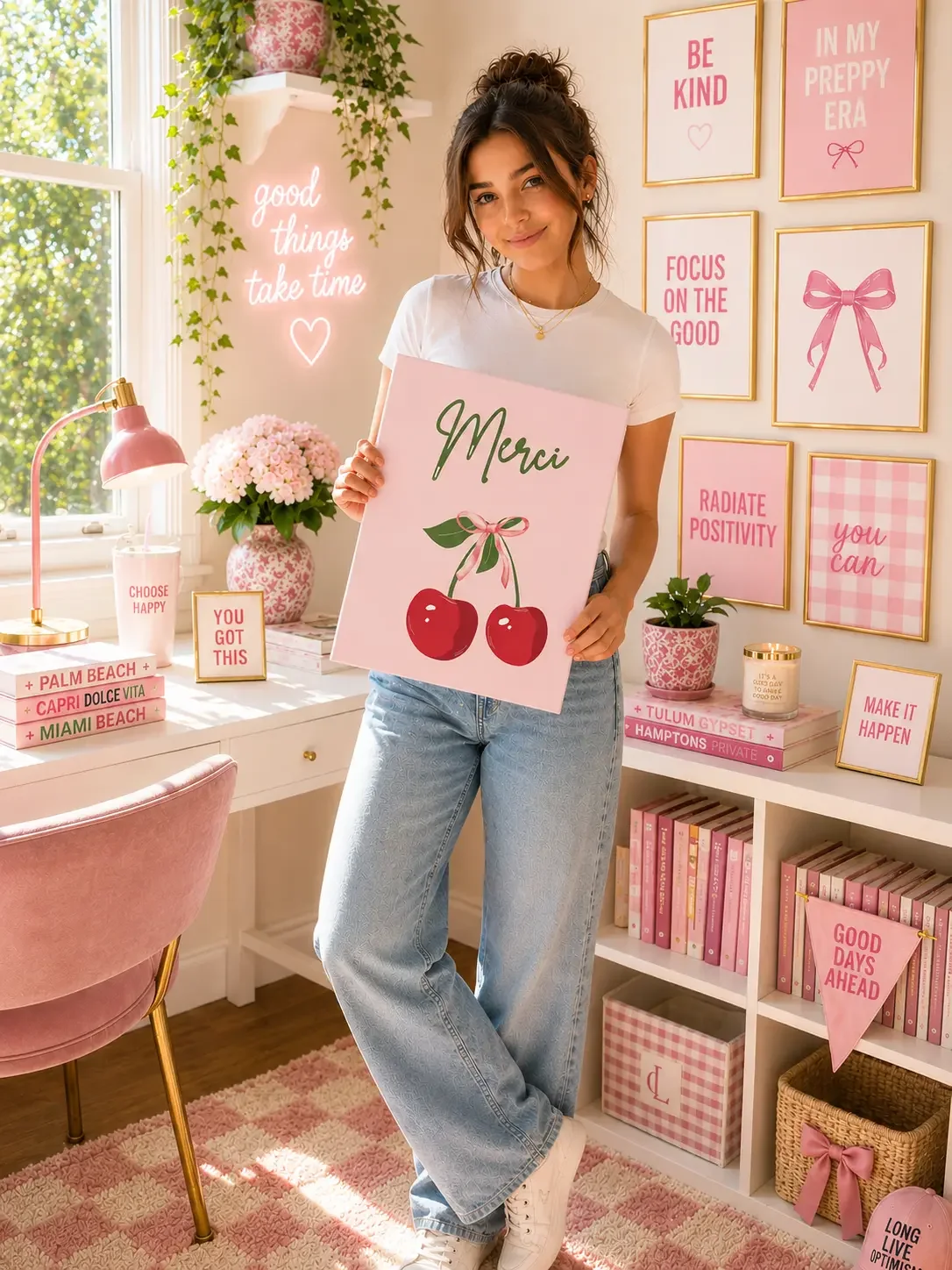Girl holding a pink "Merci" cherry canvas print in a preppy bedroom with a white desk and pink framed art.