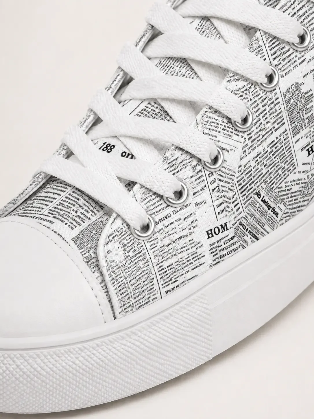 Close-up of a white canvas high-top sneaker featuring a vintage newspaper print pattern and white laces.