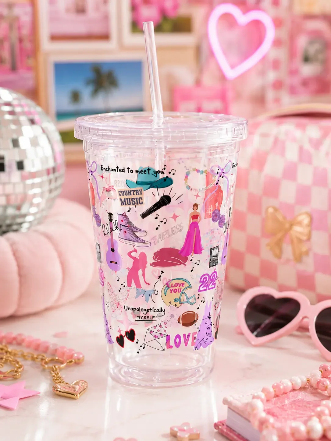 An empty preppy country music pop star doodle tumbler cup on a pink desk setup with a mini disco ball and sunglasses.