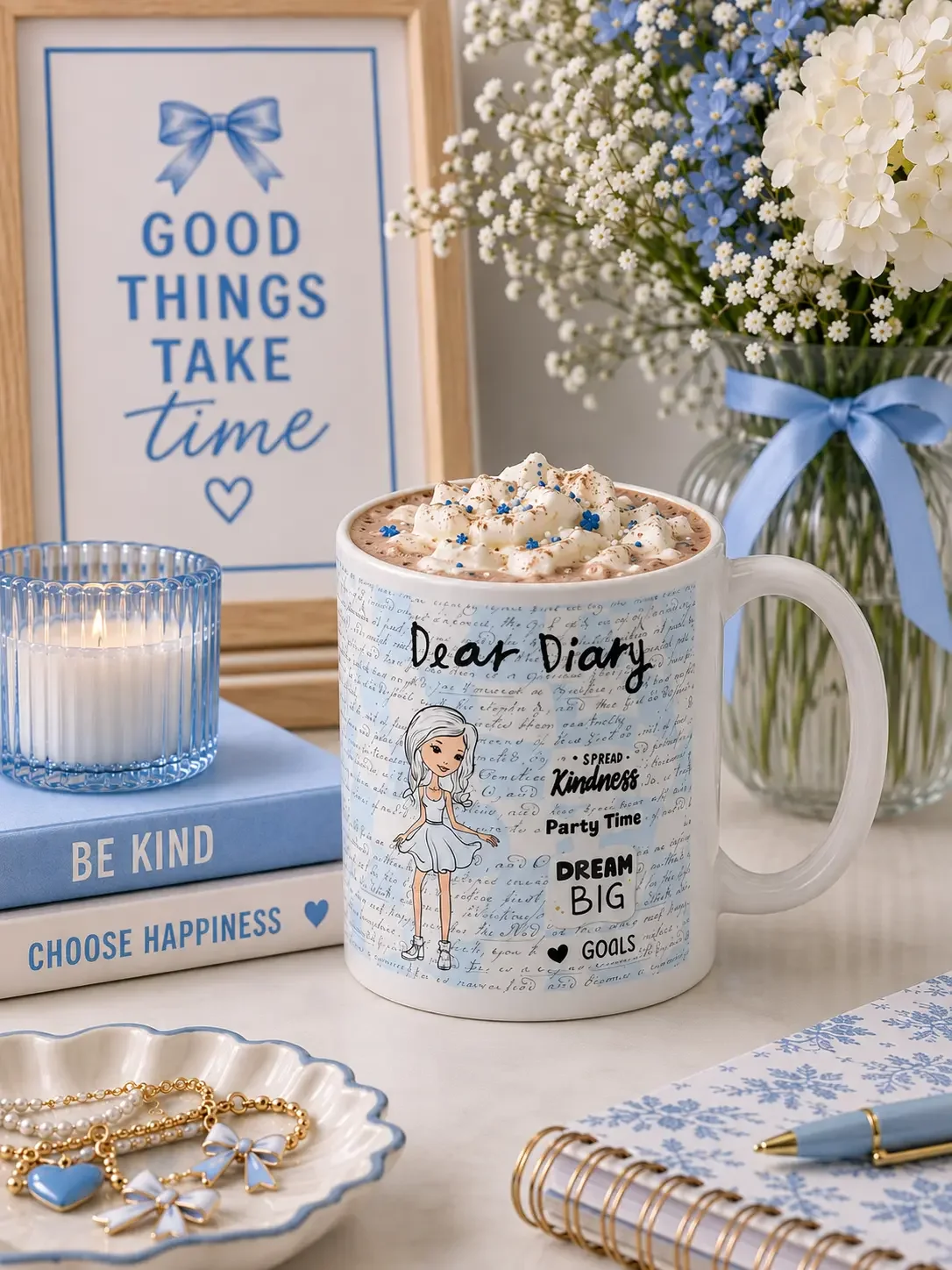 Dear Diary mug filled with whipped cream on a desk with blue books, a lit candle, and white and blue flowers.