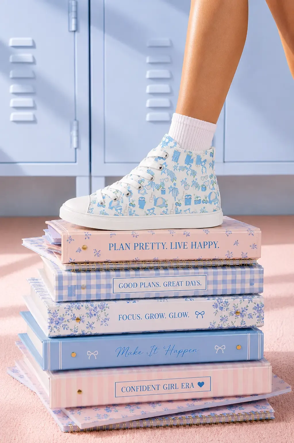 A person wearing a blue coastal charm print high-top canvas sneaker stepping on a stack of colorful blue and pink patterned binders.