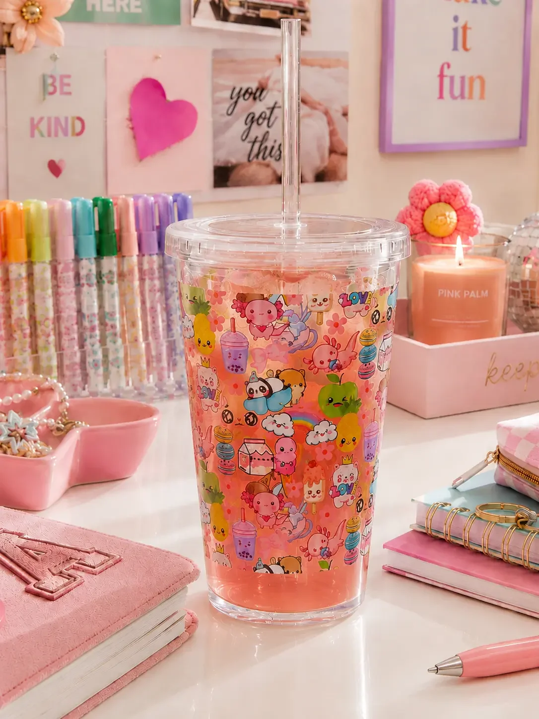 Kawaii doodle carnival cup filled with a pink iced drink on a pastel pink desk with stationery and a candle.