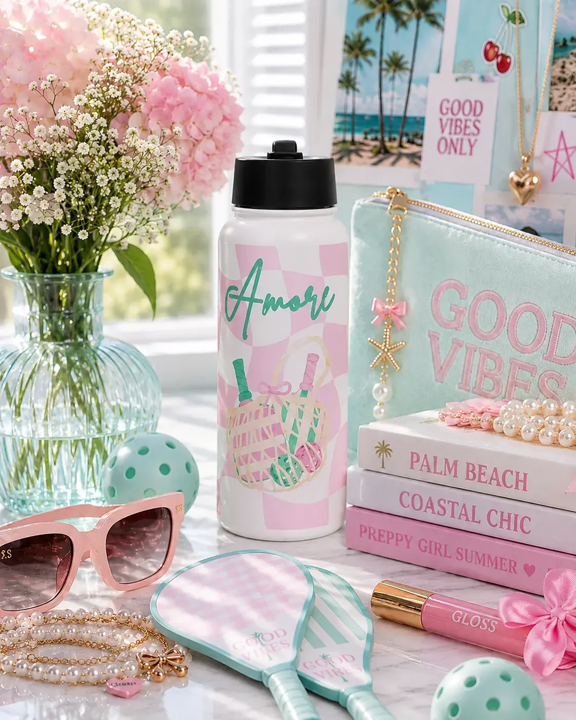 An Amore print water bottle standing next to Palm Beach books, mint pickleball paddles, and a Good Vibes pouch.