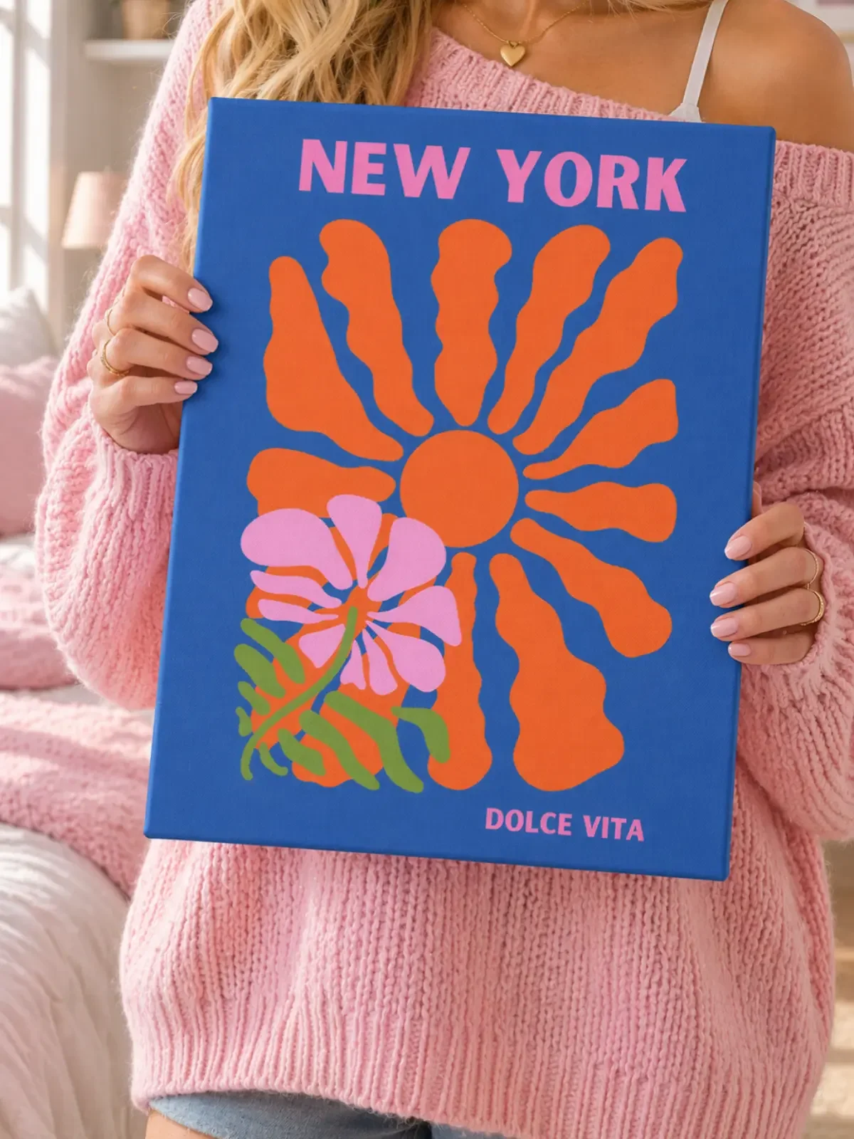 A girl in a pink sweater holds the Doodles and Saffron canvas print featuring a retro orange sun and pink flower on a blue background.
