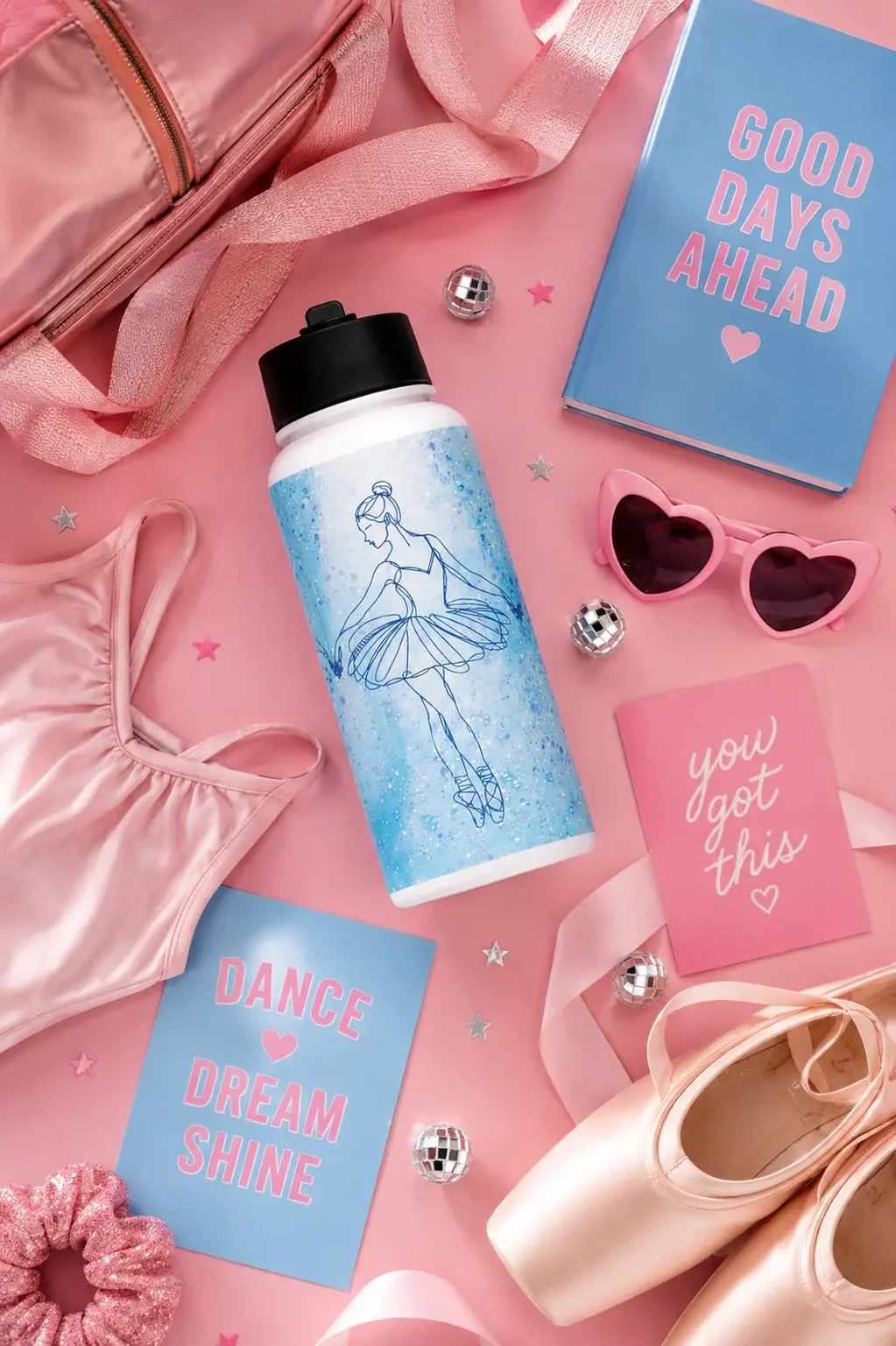 Top-down view of a blue ballerina water bottle among pink pointe shoes, a leotard, heart sunglasses, and blue notebooks.