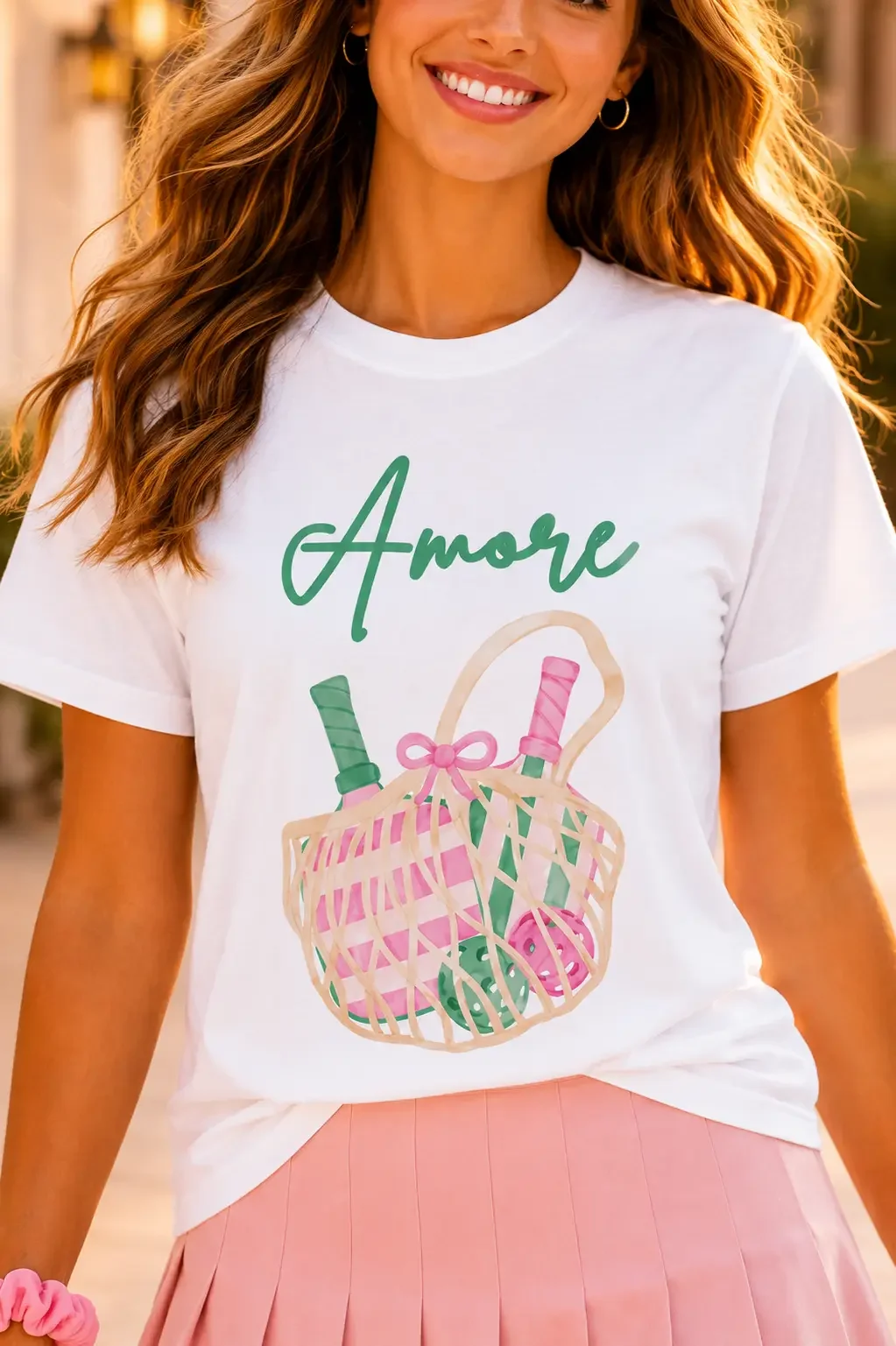 Close-up view of a white crew neck t-shirt featuring cursive green Amore text above a detailed pickleball bag graphic illustration.